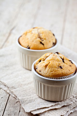 Two homemade fresh muffins on ceramic white bowls on linen napkin on rustic wooden table.