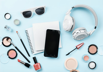 Wall Mural - Mock up woman's cosmetics, phone, headphones and glasses on blue background. Notebook and decorative cosmetics: highlighter, concealer, rouge, and brushes for face make up. Copy space. 'To do' list