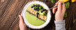 Breakfast detox green smoothie bowl from banana and spinach on wooden background. Healthy food concept with women hands and copy space, top view, banner