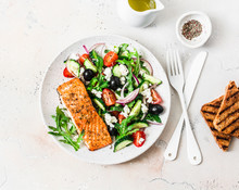 Healthy Balanced Lunch - Grilled Red Fish Fillet Salmon And Tomatoes, Cucumbers, Olives, Feta Greek Salad On A Light Background, Top View