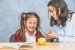 © Andrii - Mom talking to her baby. During this on a gray background. The girl cries, mom stroking her hand and talking to her daughter. Gray background. On the desk of the book and a green apple.
