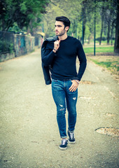 Wall Mural - One handsome young man in urban setting in modern city, standing, wearing black leather jacket and jeans, looking away