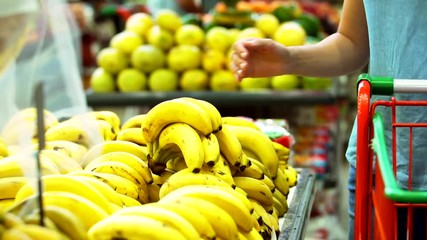 Wall Mural - Woman's hand choosing banana in supermarket. Choosing fruit.