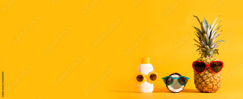 Pineapple and coconut wearing sunglasses with sunblock on a solid background - obrazy, fototapety, plakaty 