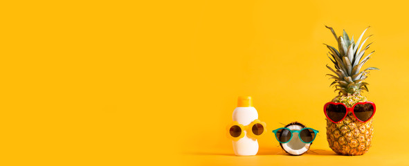 pineapple and coconut wearing sunglasses with sunblock on a solid background