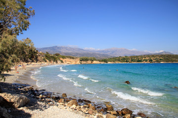 Greek island coast with clear blue sea, trees above the water by sandy beach on a summer day, south of Crete