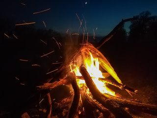 Bonfire at night by the river with sparks in the sky.