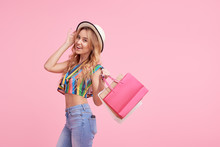 Sale Concept. Woman In Mall. Portrait Of A Happy Pretty Girl In Summer Hat Holding Shopping Bags And Looking At Camera Isolated Over Pink Background 