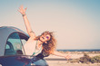 Freedom and travel happy laughing people concept with beautiful caucasian young woman out of the car enjoying the destination place opening arms and shouting free - ocean in background and sun