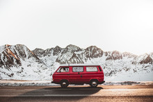 Red Camper Riding On Asphalt Countryside Road Near Snowy Mountain Ridge On Sunny Day During Trip In Nature