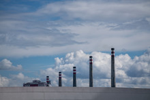 Industrial Exhaust Stacks In Row Behind Grey Wall On Background Of Cloudy Picturesque Sky