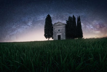 Beautiful Peaceful Landscape Of Small Chapel With Trees In Remote Empty Green Field Against Starry Sky, Italy