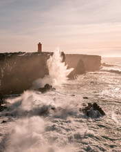 Storm Waves At The West Coast Of Iceland And Svˆrtuloft Lighthouse At The Distance