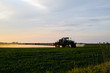 tractor with the help of a sprayer sprays liquid fertilizers on young wheat in the field.