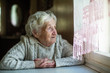 © De Visu - An elderly woman looks out the window sitting in his house. Care of lonely pensioners.