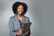 Leinwandbild Motiv Black African American teacher or businesswoman sitting and holding a tablet computer.  The confident female author or writer looks like she is preparing for a seminar or as a keynote speaker.