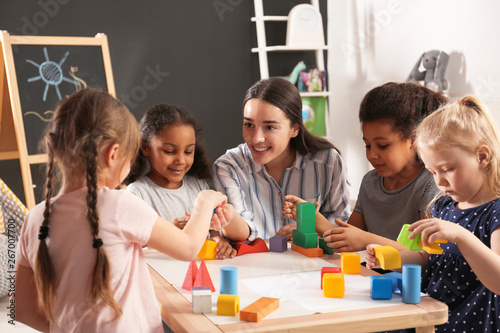 Fotografía Cute little children and nursery teacher playing with building blocks in kindergarten