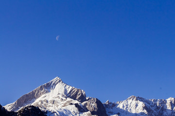 moon on the blue sky over snow covered mountain peaks