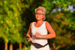 © TheVisualsYouNeed - middle aged 40s or 50s happy and attractive woman with grey hair training at city park with green trees on sunrise doing running and jogging workout in health care