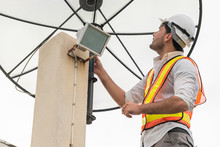 Professional Technician Or Engineer Standing On Roof Top Of Building Working With Satellite Dish. Concept Of Repair Installation Service And Telecommunication.