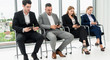 © InfiniteFlow - Businesswomen and businessmen using mobile phone while waiting on chairs in office for job interview. Corporate business and human resources concept.