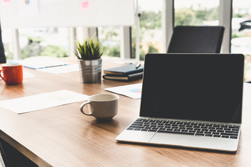 Laptop computer with opened lid on table in meeting room of office workspace.