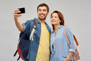 travel, tourism and vacation concept - happy couple of tourists with backpacks taking selfie by smartphone over grey background
