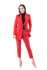 Stylish young serious modern business woman in red suit with hand in pocket looking at camera. Full body isolated on white background.