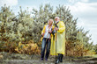 © rh2010 - Happy senior couple in yellow raincoats hiking with trekking sticks in the young pine forest. Concept of an active lifestyle on retirement