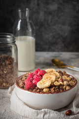 healthy breakfast granola in a plate with nuts, banana and raspberries, copy space