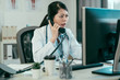 © PR Image Factory - angry asian chinese woman doctor yells into phone. mad lady medical worker has conversation with patient bad emotions. confused young girl intern frowning talking looking at computer argue in clinic.