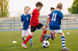 © matimix - Young Football Players Kicking Ball on Soccer Field. Soccer Horizontal Background. Youth Junior Athletes in Red and Blue Soccer Shirts