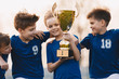 © matimix - Boys sports team celebrating victory. Happy children holding golden trophy. Kids football team raising winners' cup.  Youth sports success