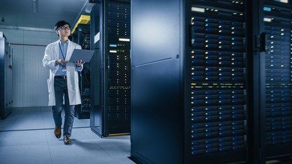 Aufkleber - In Data Center: Male IT Technician Wearing White Coat Walking alongside Server Racks, Uses Laptop Computer to Run Maintenance Diagnostics Tools. He is Wearing Lab Coat and Working with Data.