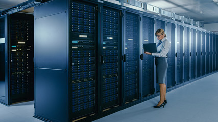 Aufkleber - In Data Center: Female IT Technician Stands Near Rack Cabinet and Runs Maintenance Program on Laptop, Controls Operational Server's Optimal Functioning. 