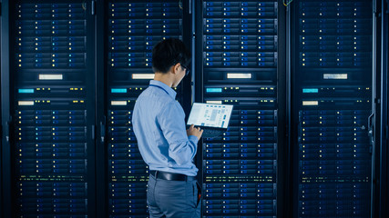 Wall Mural - In the Modern Data Center: IT Engineer Standing Beside Open Server Rack Cabinets, Does Wireless Maintenance and Diagnostics Procedure with a Laptop.