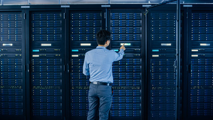 Aufkleber - In the Modern Data Center: IT Engineer Standing Beside Open Server Rack Cabinets, Does Wireless Maintenance and Diagnostics Procedure with a Laptop. He Touches Server Buttons.