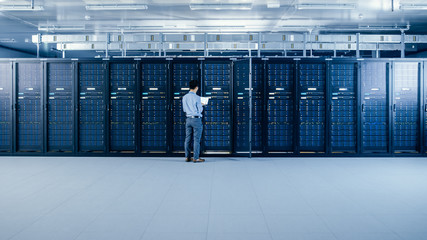 Wall Mural - In the Modern Data Center: IT Engineer Standing Beside Open Server Rack Cabinets, Does Wireless Maintenance and Diagnostics Procedure with a Laptop.