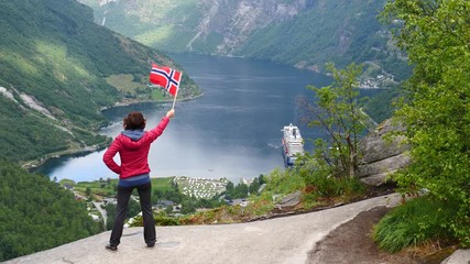 Sticker - Tourist woman holding norwegian flag, enjoying Geirangerfjord fjord view with large cruise ship. Tourism, travel for relaxation and sightseeing