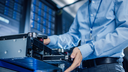 In the Modern Data Center: IT Engineer Installs New HDD Hard Drive and Other Hardware into Server Rack Equipment. IT Specialist Doing Maintenance, Running Diagnostics and Updating Hardware.