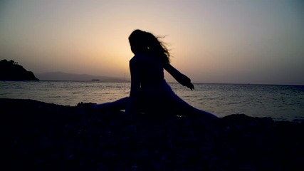 Wall Mural - Silhouette di una bambina che fa passi di danza al tramonto sulla spiaggia di fronte al mare.