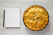 Homemade apple pie and blank notepad with pencil on a white wooden background, top view. Flat lay, overhead, from above.