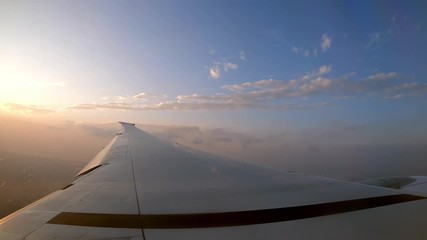 Wall Mural - 4K, Beautiful twilight and clouds from above. Wing of the plane and the orange sunset as seen through an airplane window during the flight. Passenger POV traveling by air.-Dan