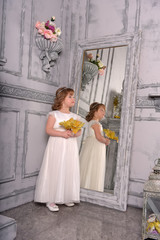 a girl in a white dress with a funny facial expression and a big Christmas gold flower at the mirror and a reflection