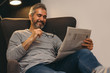 © cherryandbees - middle aged happy man reading newspaper relaxed in his sofa at home