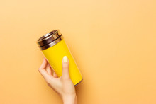 Female Hand Holding A Yellow Empty Thermocup For Drinks On A Warm Yellow Background