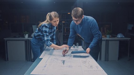 Poster - In the Dark Industrial Design Engineering Facility Male and Female Engineers Talk and Work on a Blueprints Using Conference Table. On the Desktop Drawings, Drafts and Electric Engine Components, Parts