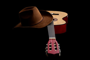 Fototapete - American culture, folk song and country muisc concept theme with a cowboy hat and an acoustic guitar isolated on black background with dramatic lighting