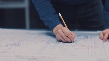 Poster - In the Dark Industrial Design Engineering Facility: Male Engineer Works with Blueprints Laying on a Table, Uses Pencil, Ruler and Digital Tablet. On Desktop Multiple Drawings. Focus on Hands