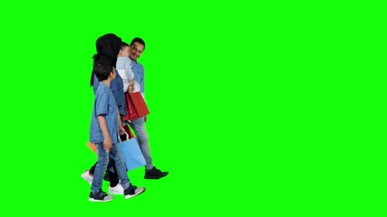 Wall Mural - Side view of happy muslim family carrying shopping bags while walking in the studio. Shot in 4k resolution with green screen background